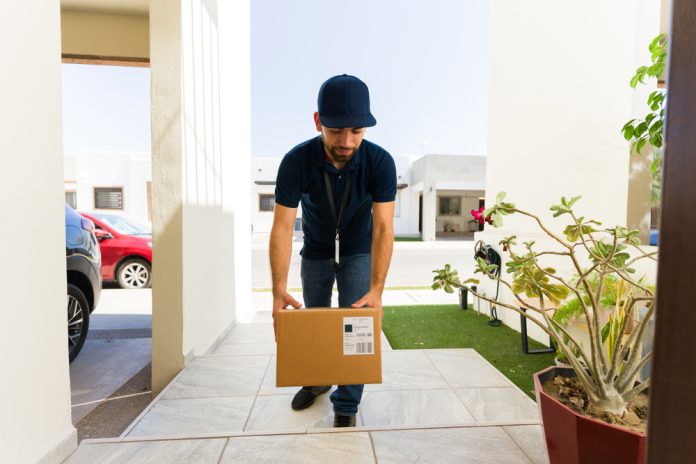 Delivery man in uniform carefully drops off a package at a house entrance, showcasing the importance of efficient logistics in online shopping